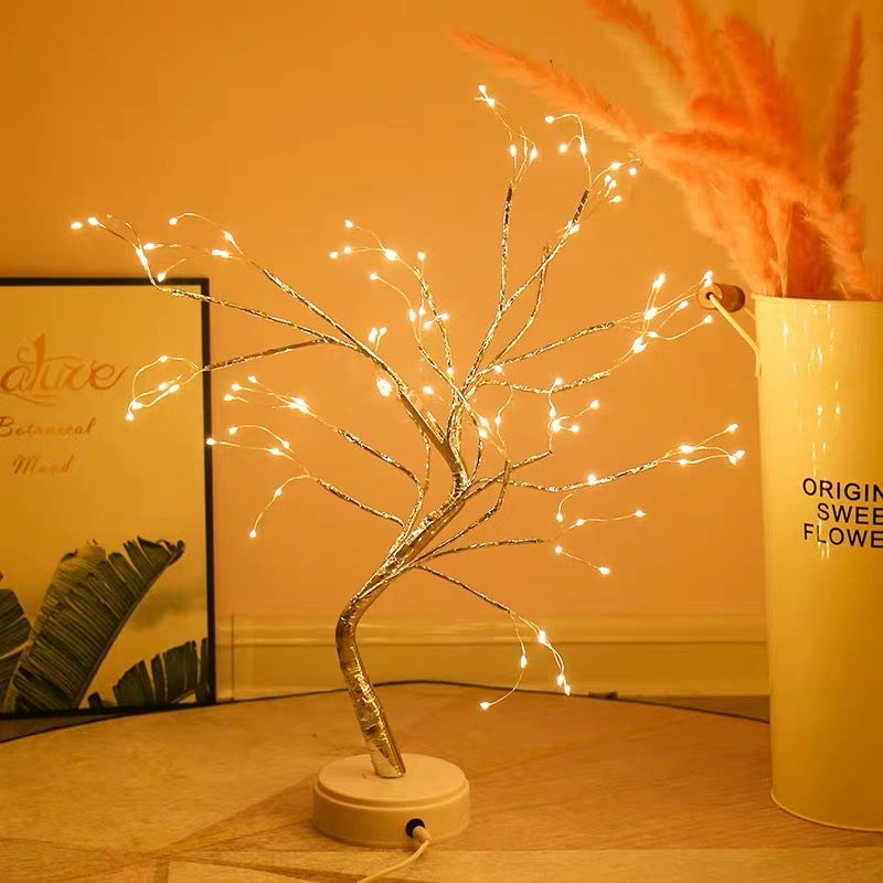 Decorative LED tree on a table with a warm glow, next to a vase with flowers and a framed picture. - Lioré® USA