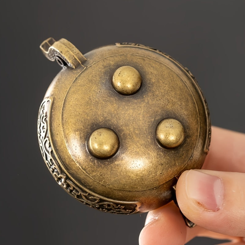 Close-up of a hand holding a decorative brass object with three raised spheres against a dark background - Lioré®