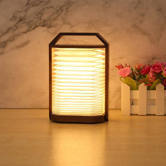 Wooden lantern-style lamp emitting warm light on a wooden surface with a blurred floral arrangement in the background. - Lioré® USA
