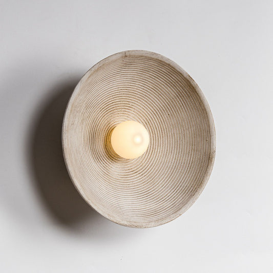 Round wall sconce with textured design on a light gray background -Lioré® USA